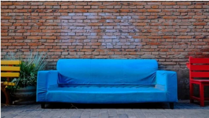 green sofa and wooden side chairs in front of a brick wall