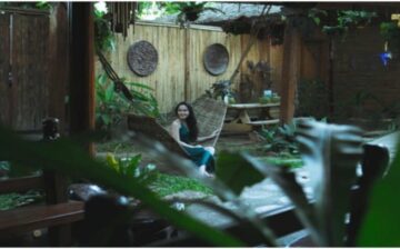 woman sitting on hammock in yard surrounded by plants