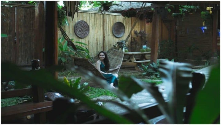 woman sitting on hammock in yard surrounded by plants