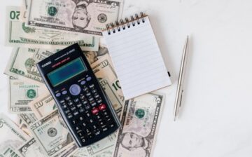 calculator, notepad, and pen over a pile of cash