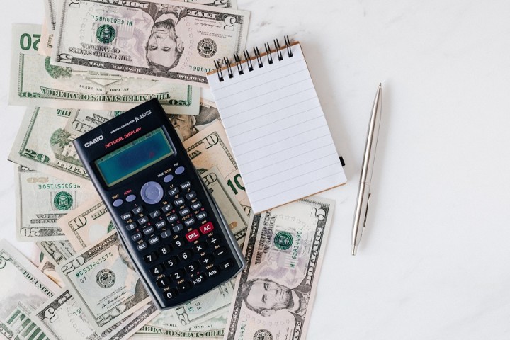 calculator, notepad, and pen over a pile of cash