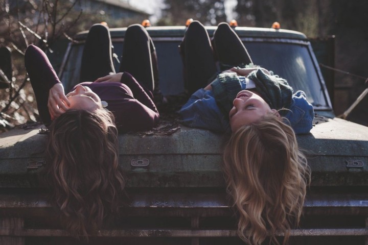 two young women talking while lying on a truck hood