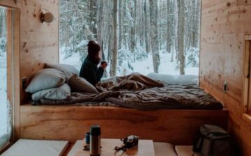 woman in bed looking out a window at a snowy forest