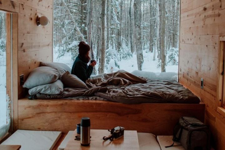 woman in bed looking out a window at a snowy forest