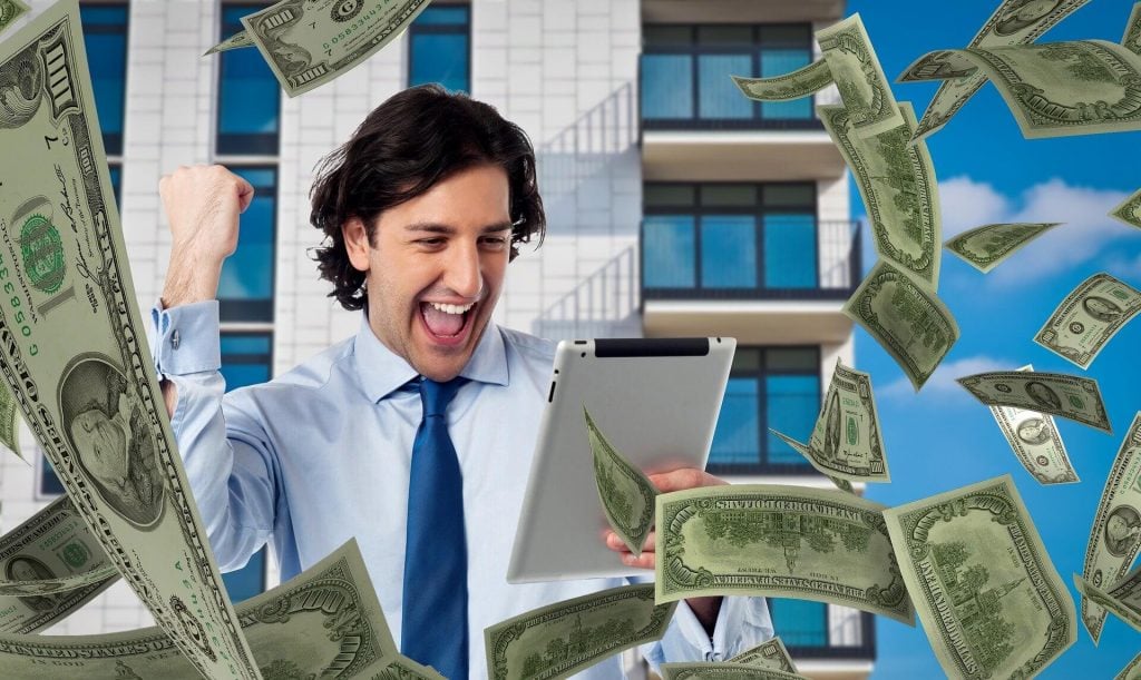 smiling man holding tablet with falling $100 bills