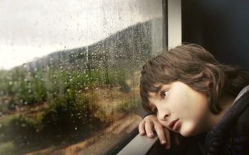 Sad looking kid gazing out of a window while travelling