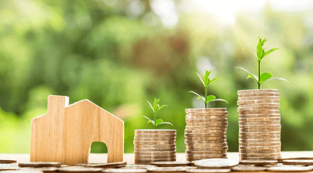 stacks of coins with plants growing out of the tops next to a model of a house