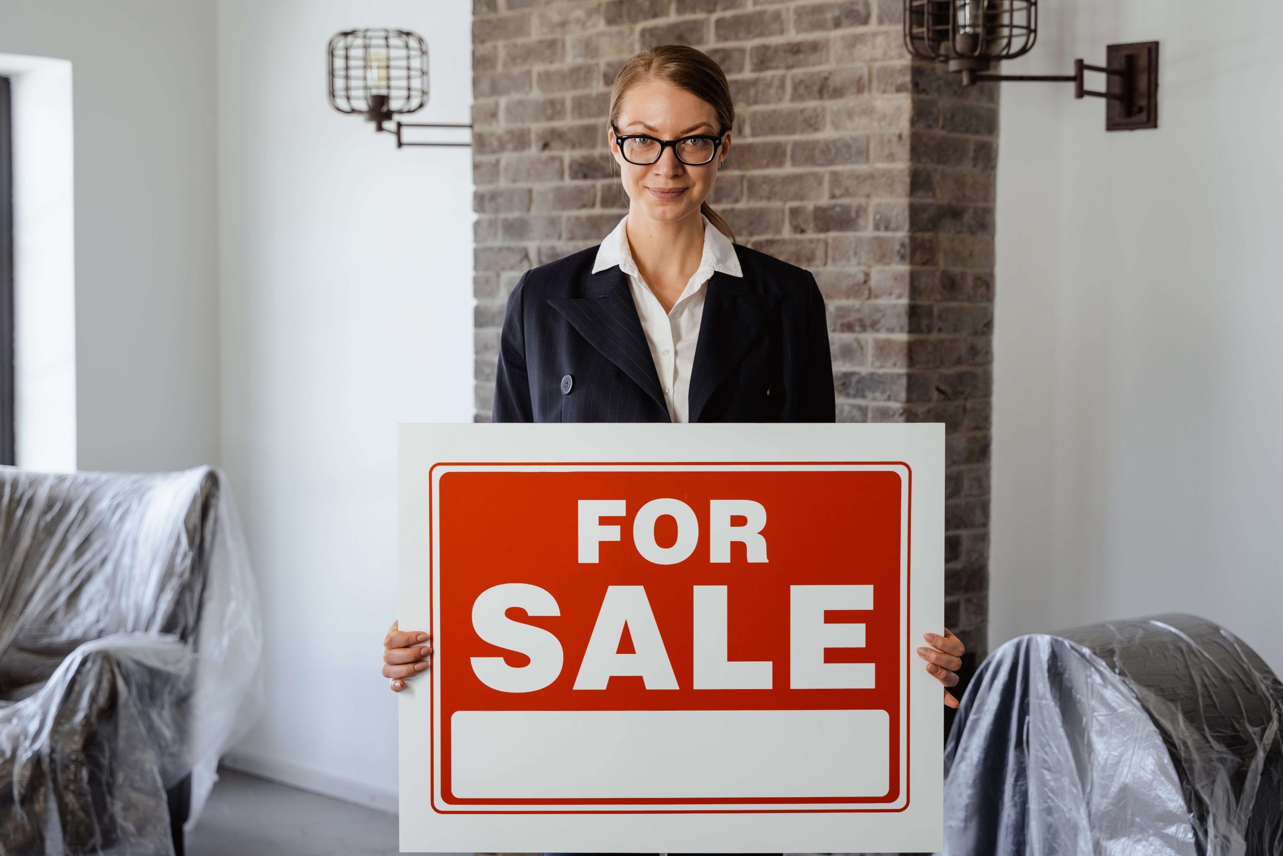 realtor in front of a house holding a For Sale sign