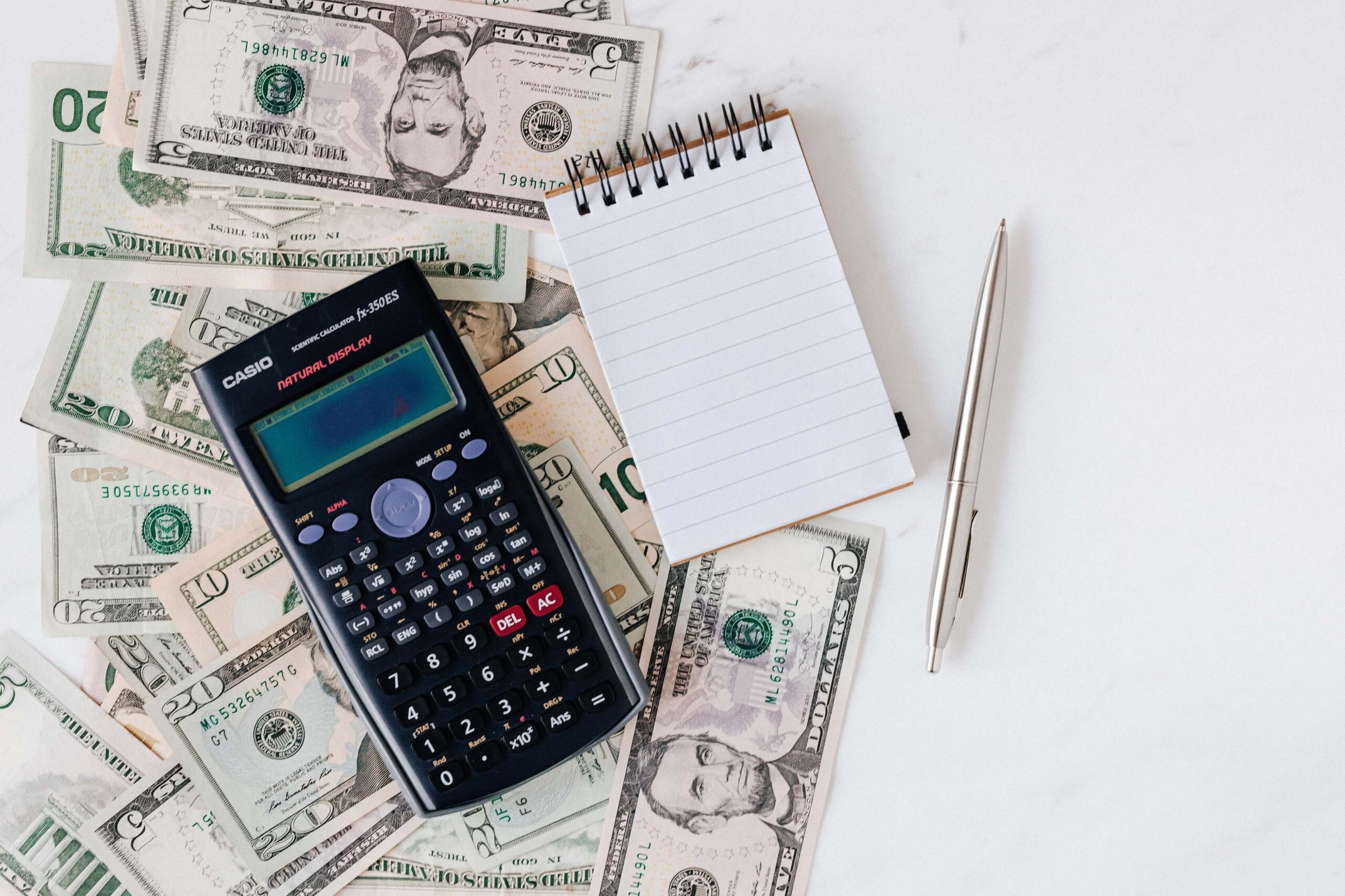 calculator, notepad, and pen on top of currency