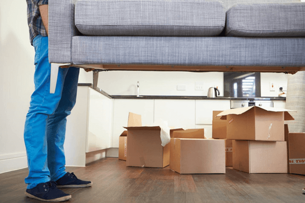 man helping lift a sofa with cardboard boxes in background