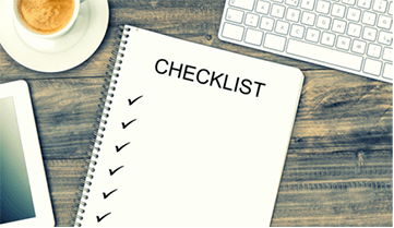 notebook with checklist next to keyboard and cup