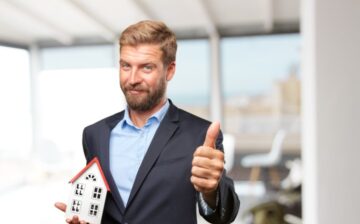 property manager in a suit showing thumbs up and holding a model house