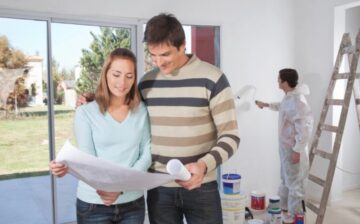 couple looking at plans of their new house and man painting behind
